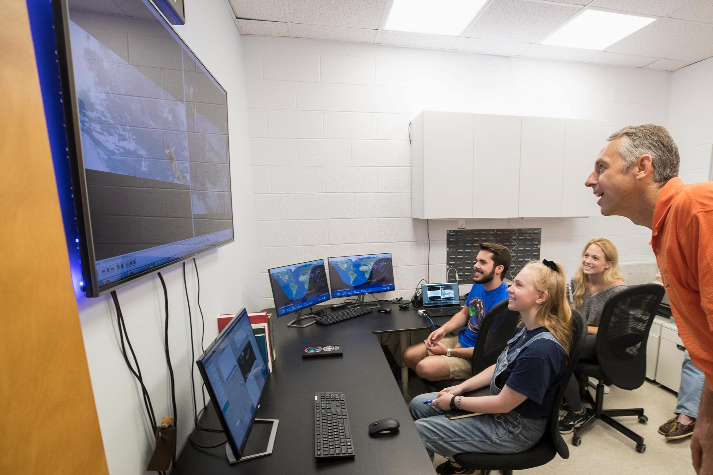 Connor Segal, left, Hannah Umansky and Kathryn Wason watch the recent deployment of Libertas from the International Space Station with professor Chris Goyne.